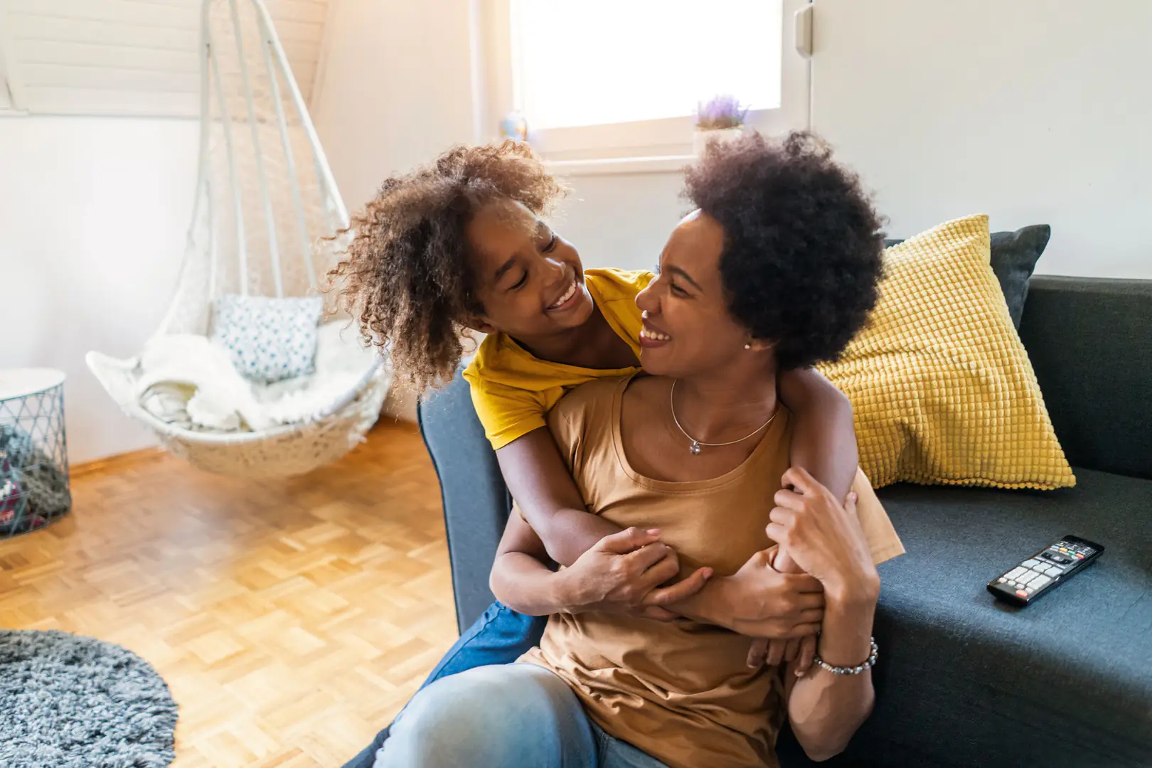 mère, fille, étreinte, sourire, joie, famille, affection, complicité, intérieur, salon, canapé, jaune, marron, parquet, chaise, cosy, coussin, télécommande