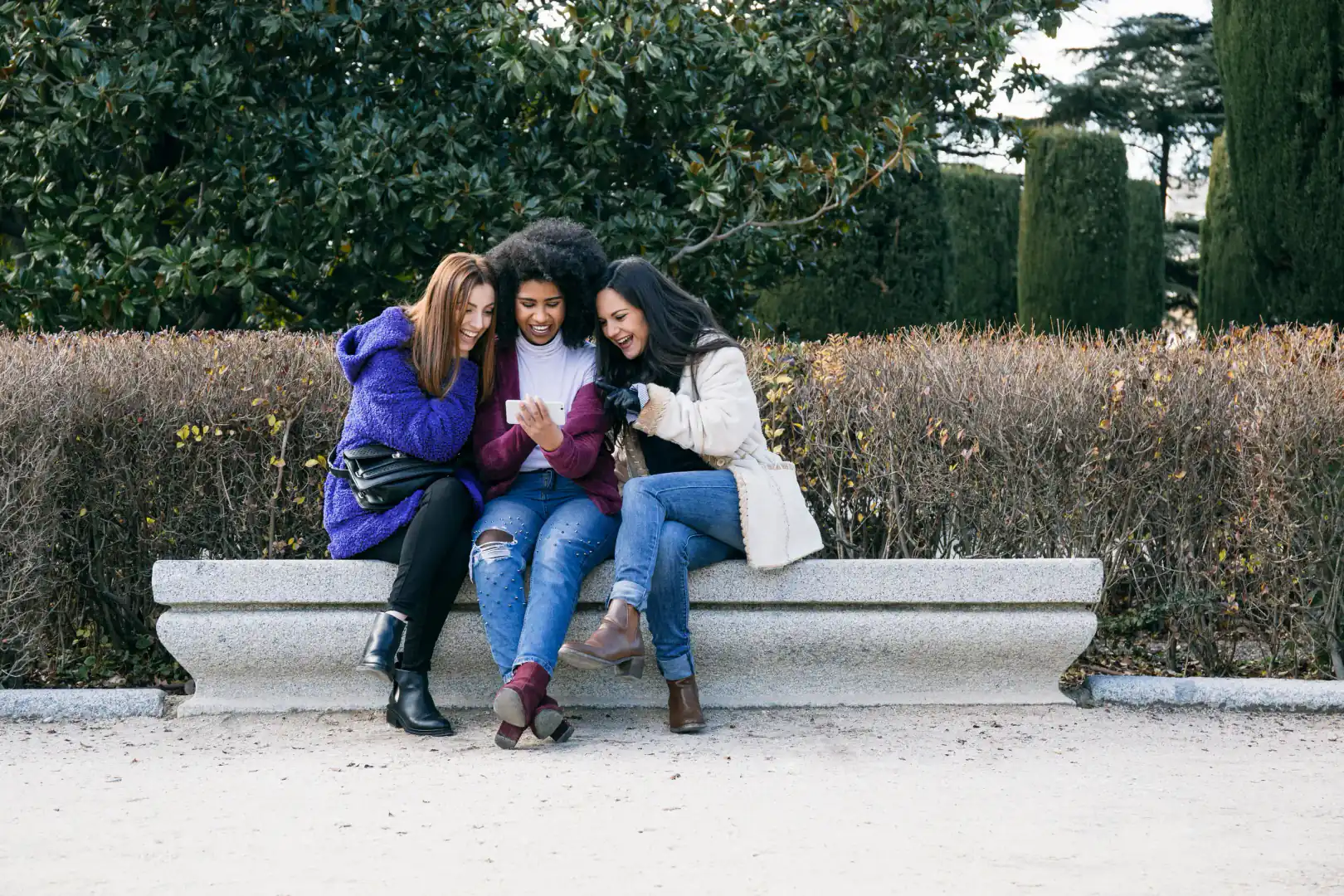 femme, rire, amitié, smartphone, partage, parc, banc, extérieur, groupe, sourire, manteau, jeans, vert, marron, hiver, violet, bleu, blanc