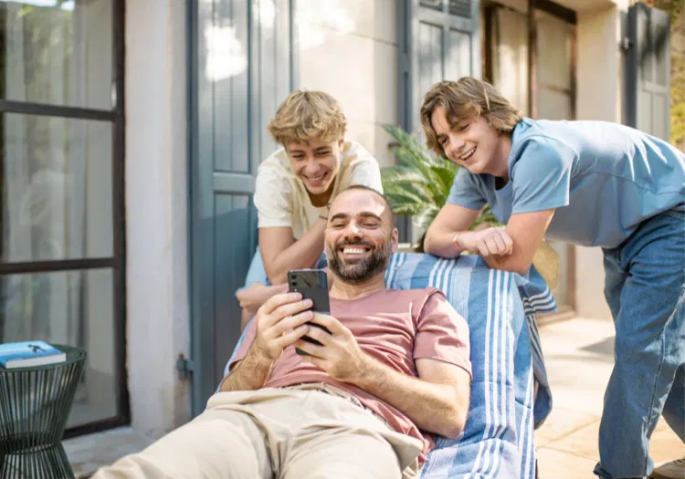 Homme sur son smartphone, ses deux fils regardent l’écran en souriant