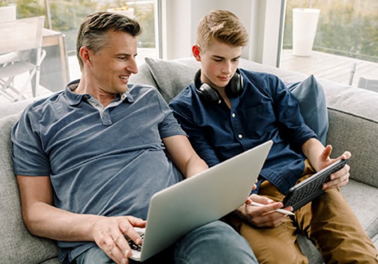 Un homme sur son ordinateur regarde ce que son fils lui montre sur sa tablette