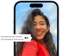 Un iPhone 15 affichant une annonce VoiceOver décrivant le contenu d’une photographie en ces termes : une personne aux cheveux noirs ondulés en train de rire