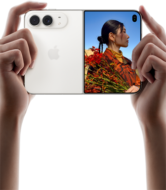 iPhone Duo, finition blanc stellaire, tenu à deux mains en position horizontale, déplié, le volet extérieur gauche présente les caméras arrière Fusion 48 MP, le volet extérieur droit présente l’écran externe affichant une personne qui se fait photographier et peut voir son propre visage pendant la prise de vue à l’aide de Duo Preview