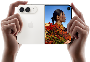 iPhone Duo, finition blanc stellaire, tenu à deux mains en position horizontale, déplié, le volet extérieur gauche présente les caméras arrière Fusion 48 MP, le volet extérieur droit présente l’écran externe affichant une personne qui se fait photographier et peut voir son propre visage pendant la prise de vue à l’aide de Duo Preview